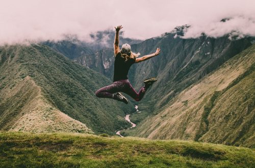 woman jumping on green mountains