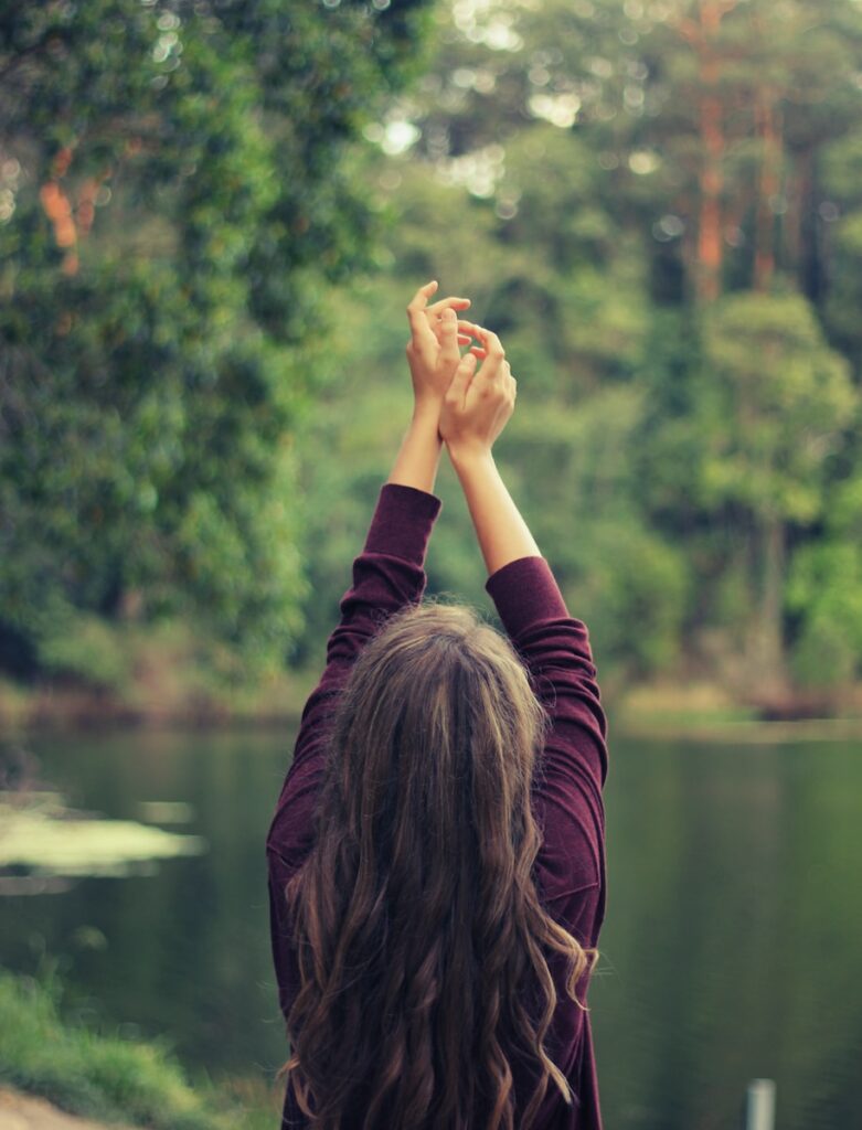 femme avec les mains en l'air devant un lac