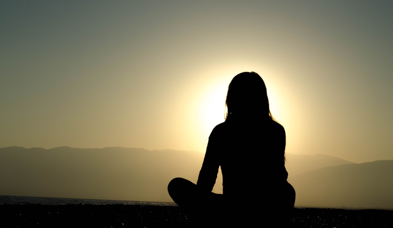 femme assise dans le sable avec le lever du soleil