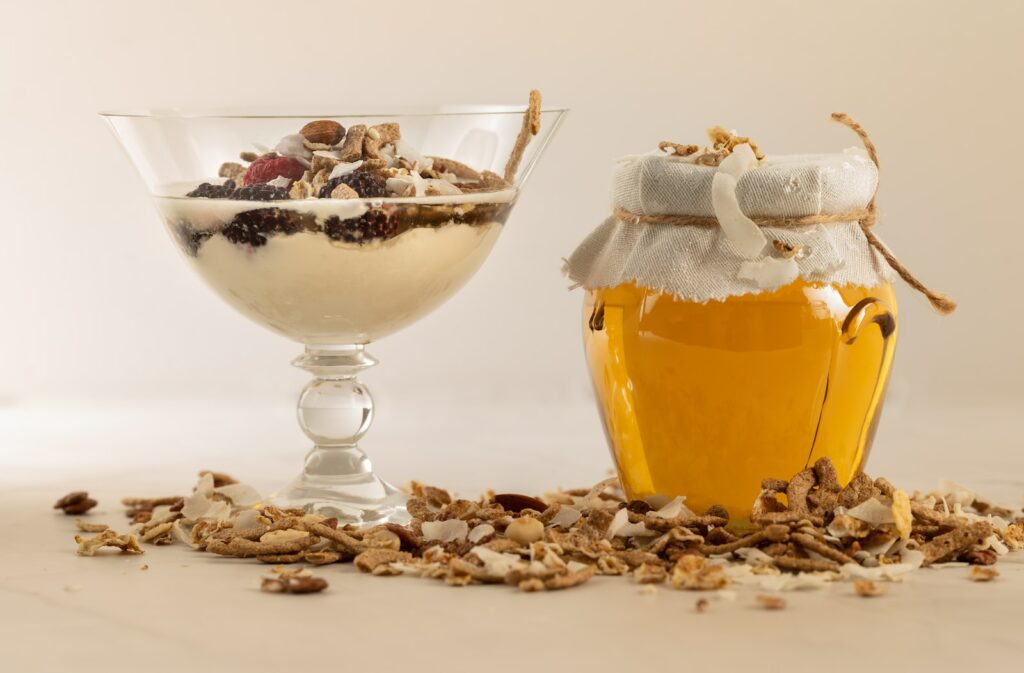 a glass of yogurt and a jar of granola with honey