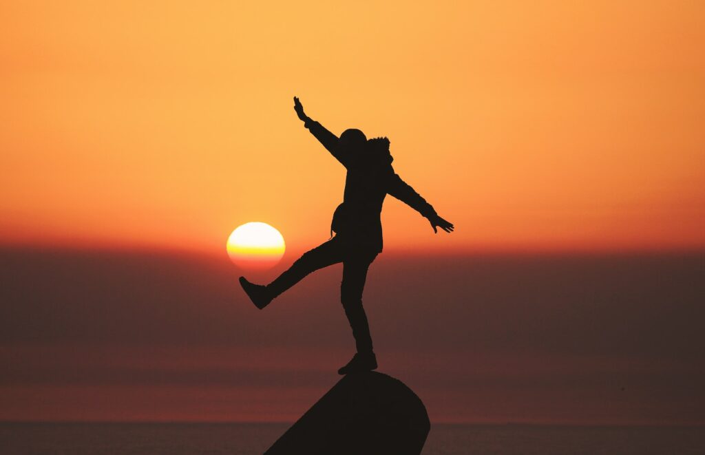 équilibre de vie, life balance, homme qui tient à une jambe sur une roche devant un coucher de soleil