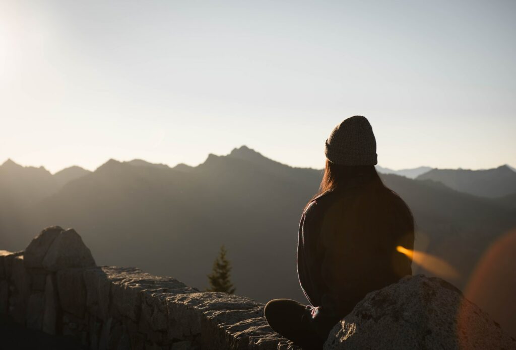 femme assise sur ds rochers devant le coucher de soleil