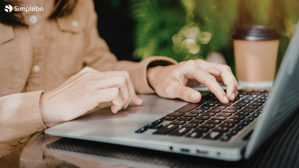 Création de site web avec Simplébo en déplacement : mains tapant sur un ordinateur portable depuis une terrasse de café en plein air.